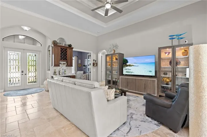 Living room with crown molding, a tray ceiling, a ceiling fan, french doors, and stone tile flooring