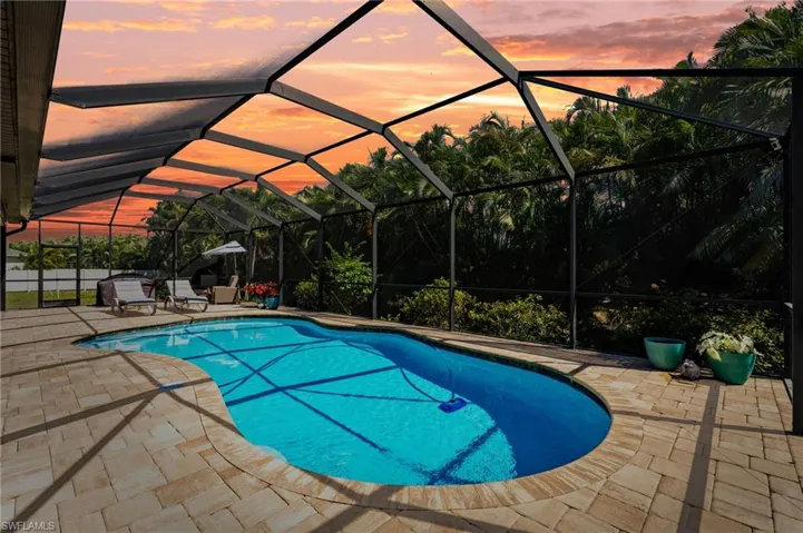 Pool at dusk with an outdoor pool, a patio, and glass enclosure