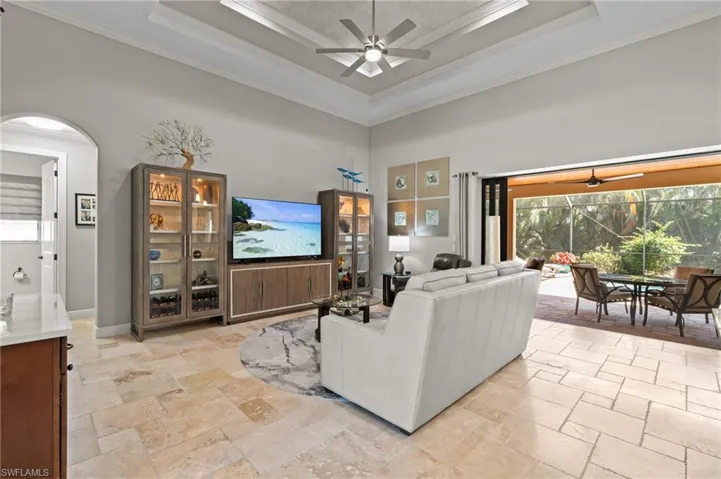 Living area with crown molding, ceiling fan, a tray ceiling, a towering ceiling, and stone tile flooring
