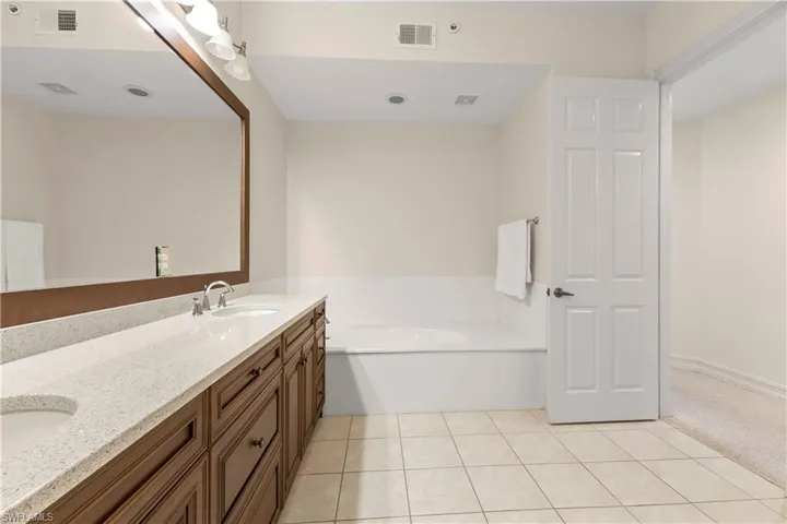 Full bathroom featuring a bath, double vanity, light tile patterned floors, and light carpet