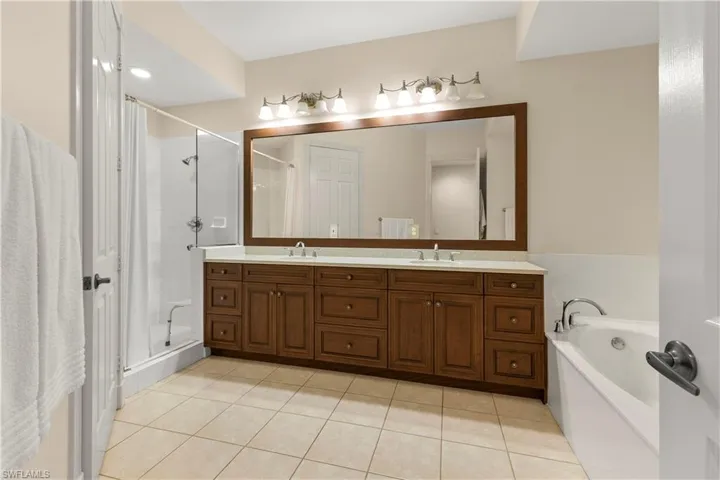 Full bathroom featuring a bath, double vanity, light tile patterned floors, and a shower stall