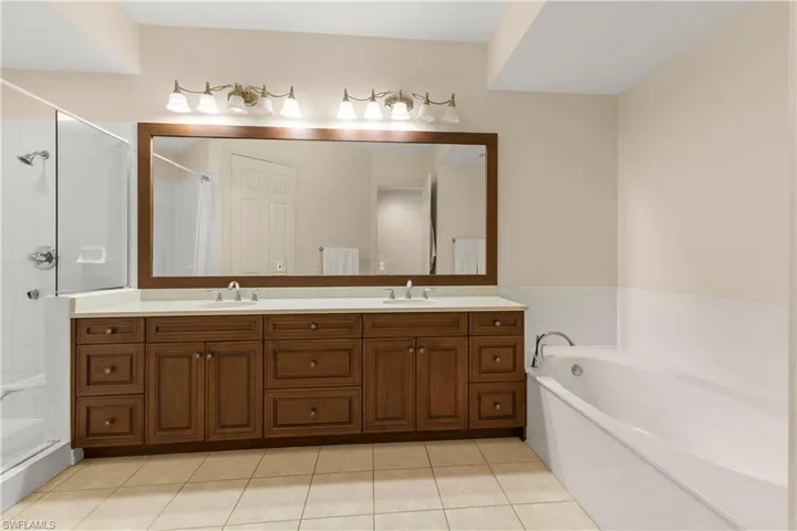 Full bath featuring double vanity, a bath, light tile patterned floors, and a tile shower