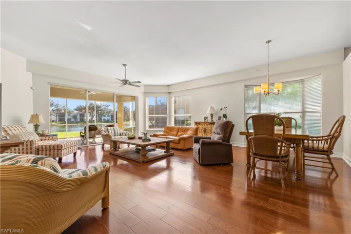 Living room featuring dark wood-type flooring, a ceiling fan, a chandelier, and a water view