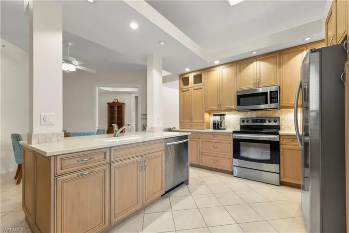 Kitchen with stainless steel appliances, recessed lighting, glass insert cabinets, light tile patterned floors, and light stone counters