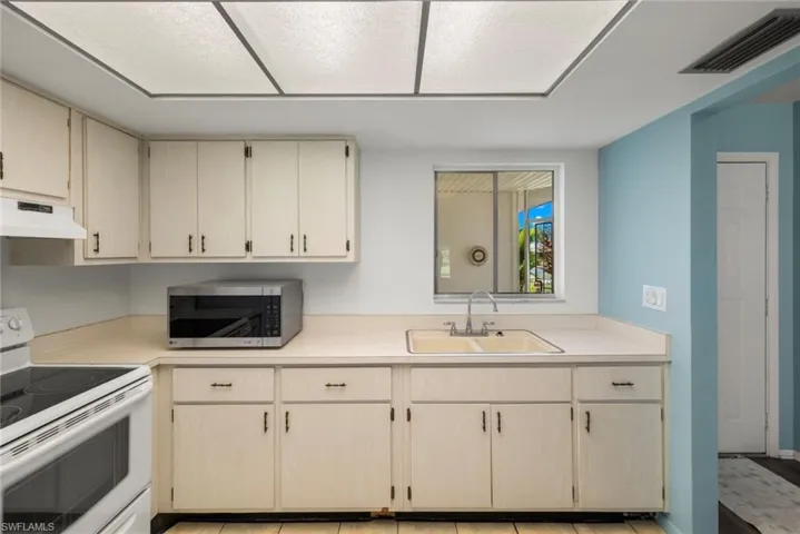 Kitchen featuring sink, light brown cabinetry, white electric range oven, and premium range hood