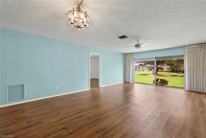 Empty room featuring a textured ceiling, ceiling fan with notable chandelier, and hardwood / wood-style flooring
