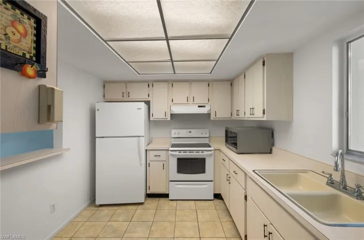 Kitchen featuring light tile patterned flooring, cream cabinetry, sink, and white appliances