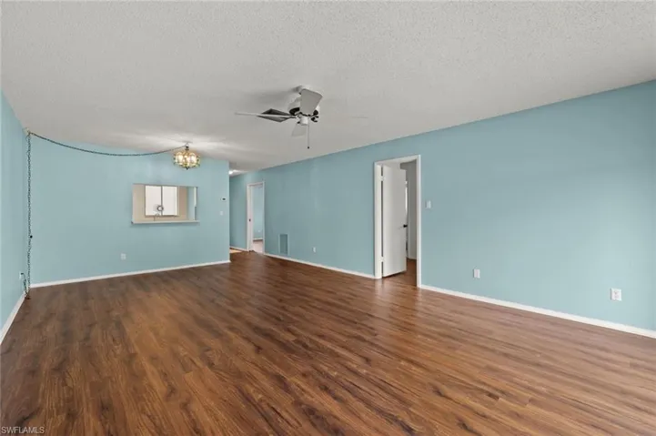 Spare room with a textured ceiling, ceiling fan with notable chandelier, and hardwood / wood-style floors