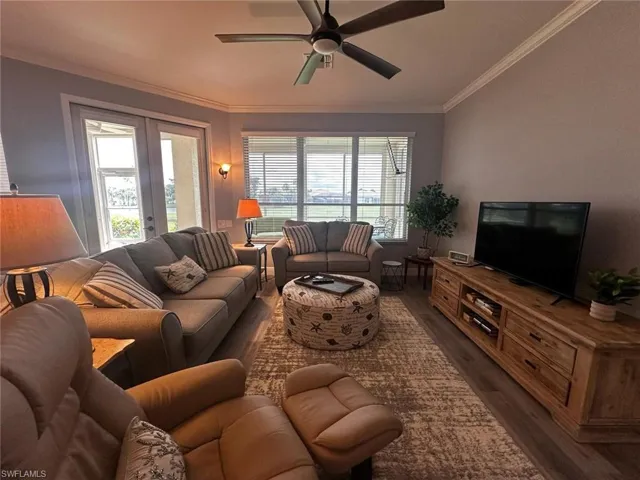 Living room with dark wood-style flooring, crown molding, ceiling fan, healthy amount of natural light, and french doors