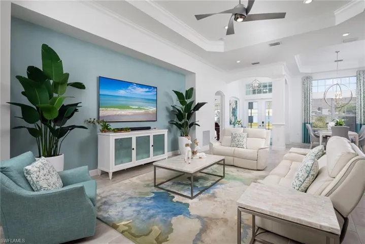 Living area with french doors, arched walkways, a chandelier, a raised ceiling, and crown molding