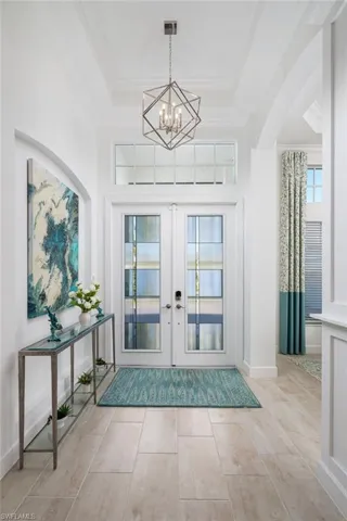 Foyer entrance featuring french doors, crown molding, a raised ceiling, a chandelier, and arched walkways