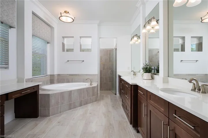 Primary bath featuring a bath, double vanity, a stall shower, and ornamental molding