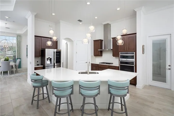 Kitchen with dark brown cabinetry, decorative light fixtures, a kitchen breakfast bar, ornamental molding, and stainless steel appliances