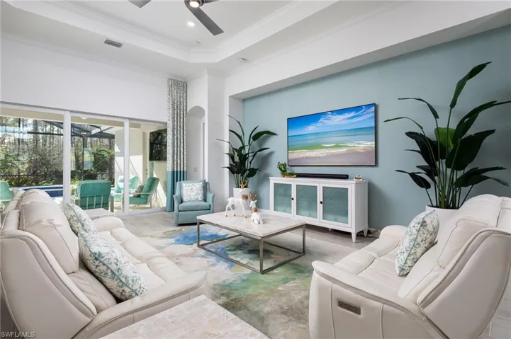 Living area featuring a ceiling fan, a raised ceiling, ornamental molding, arched walkways, and a high ceiling