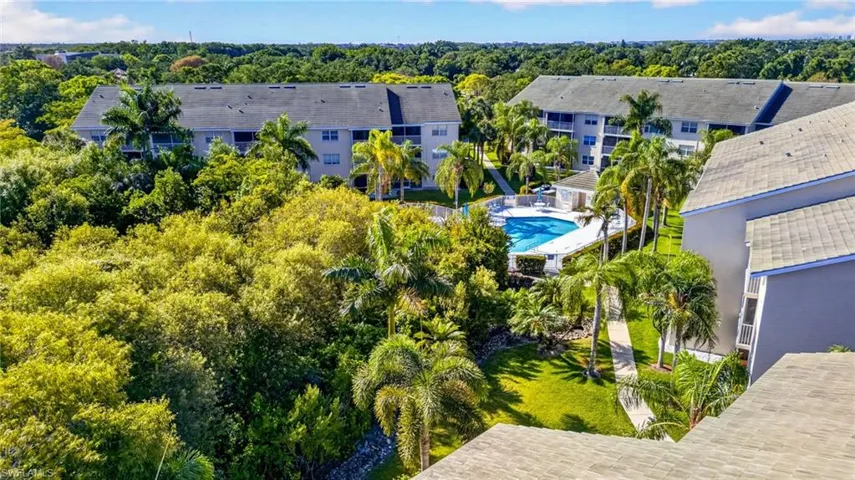 Community pool surrounded by tropical landscaping, multiple residential buildings, and walking paths