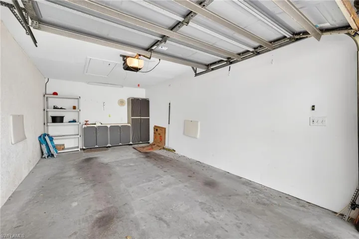 Concrete floor garage with overhead door mechanism, built-in wall shelving, integrated cabinetry, and overhead lighting