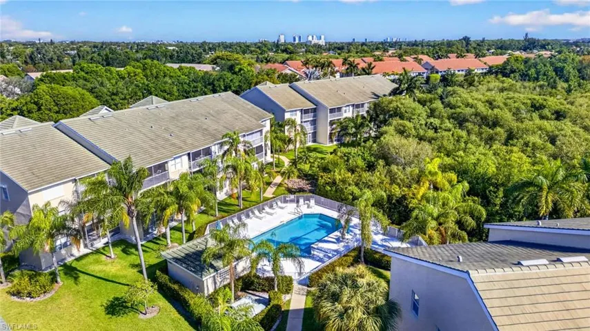 Community pool with surrounding lounge area, multiple multi-story residential buildings with balconies, mature palm trees, and manicured green spaces