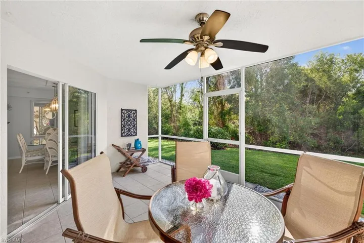 Screened lanai featuring tile flooring, a ceiling fan with integrated lighting, and a verdant backdrop