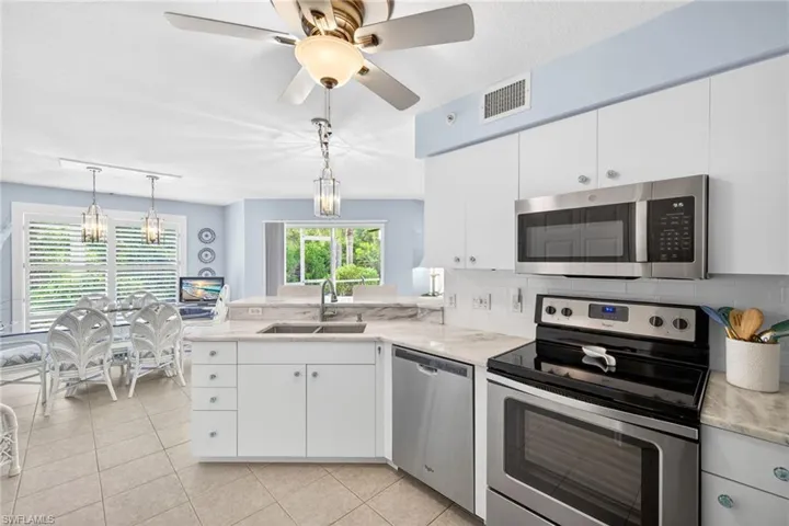 Open-concept kitchen featuring white cabinetry, stone countertops, stainless steel appliances, and tile flooring