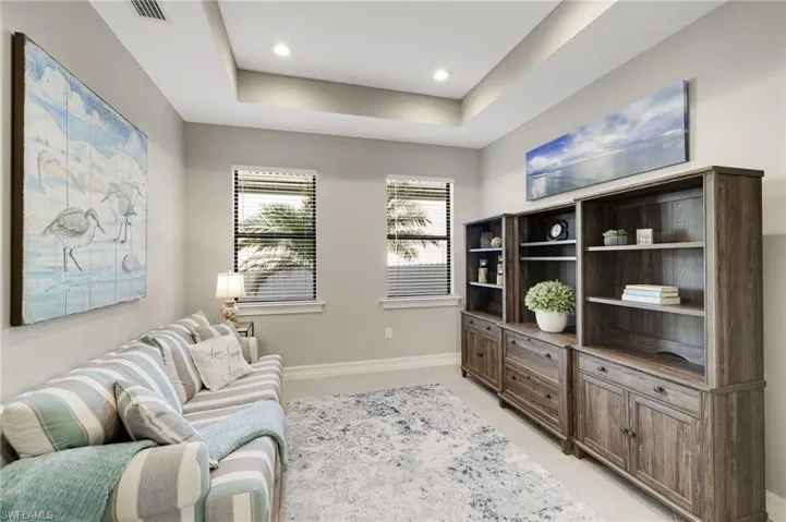 The centrally located den features a tray ceiling with recessed lighting, tile flooring, and windows that allow for abundant natural light, making it an ideal space for relaxing or entertaining.