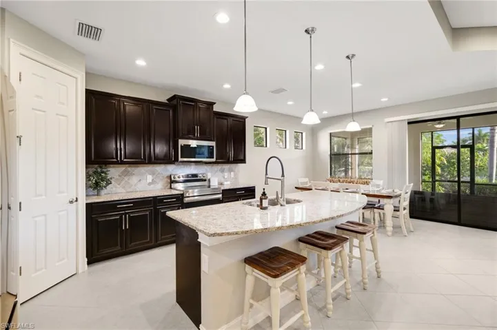 The kitchen is truly a dream, offering brand-new stainless steel appliances, warm wood cabinetry, ample counter space, and a spacious center island with breakfast bar seating, highlighted by recessed lighting and pendant lighting over the island.