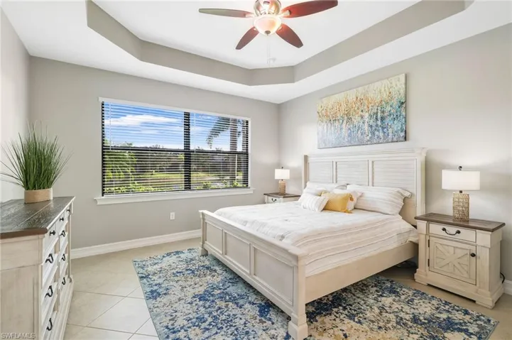 The primary bedroom suite features a tray ceiling with a ceiling fan, tile flooring, and a large window showcasing stunning water views.