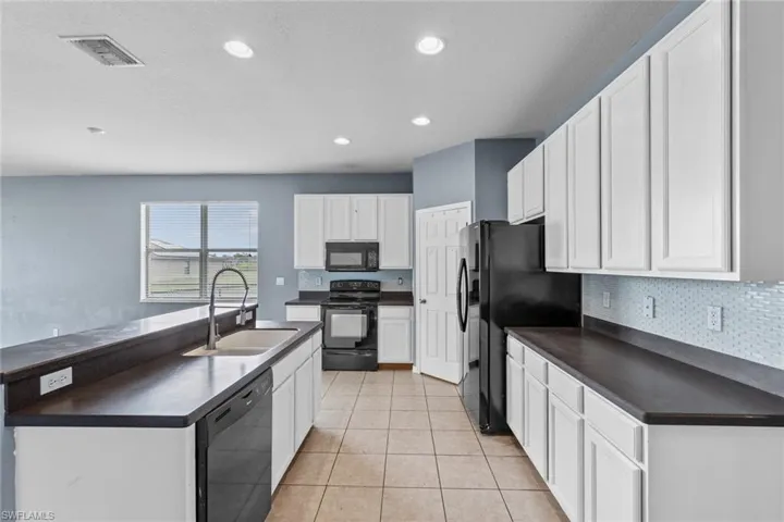 Kitchen featuring dark countertops, white cabinets, black appliances, recessed lighting, and light tile patterned floors