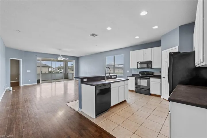 Kitchen with dark countertops, a kitchen island with sink, black appliances, open floor plan, and white cabinets
