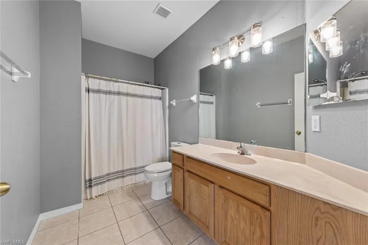 Full bath with a textured wall, vanity, a shower with curtain, and light tile patterned flooring