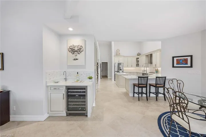 Indoor wet bar featuring decorative backsplash, wine cooler, light stone counters, cream cabinets, and glass insert cabinets