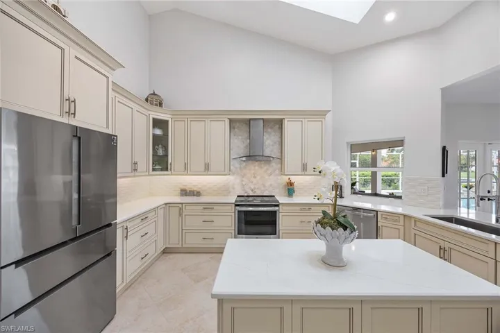 Kitchen with cream cabinets, appliances with stainless steel finishes, light stone counters, a skylight, and wall chimney range hood