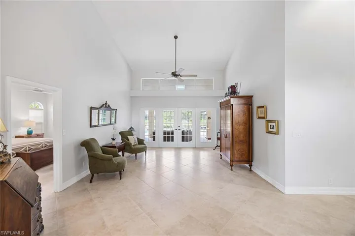 Living area with french doors, a towering ceiling, a ceiling fan, and light tile patterned floors