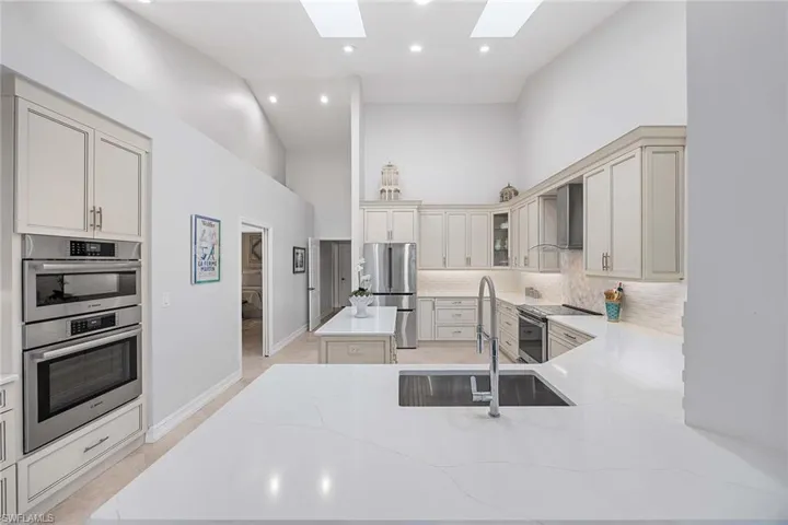 Kitchen featuring high vaulted ceiling, light stone counters, appliances with stainless steel finishes, wall chimney range hood, and recessed lighting