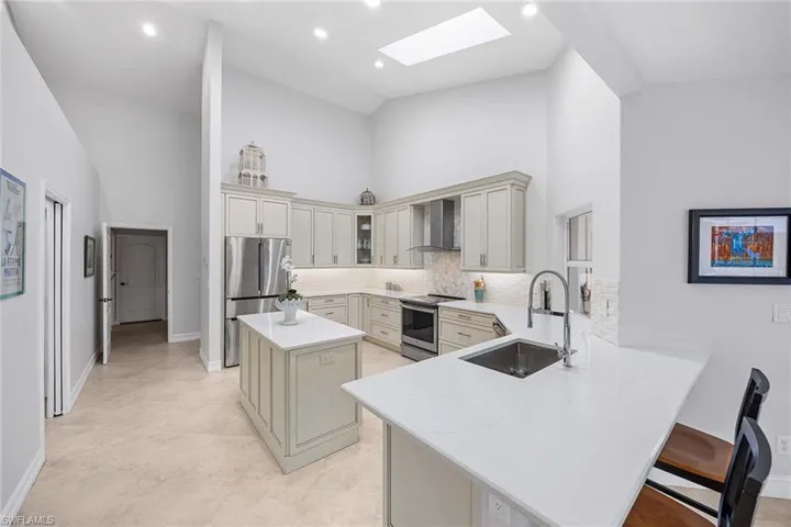 Kitchen featuring high vaulted ceiling, a skylight, appliances with stainless steel finishes, light stone countertops, and decorative backsplash