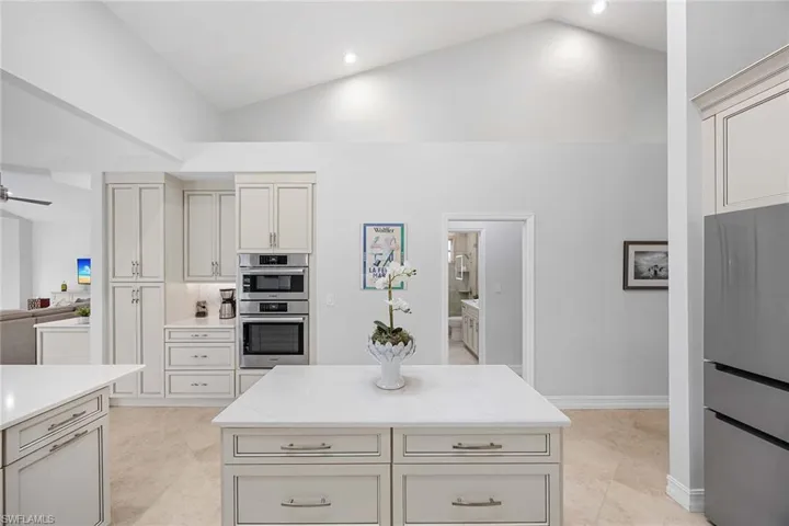 Kitchen featuring stainless steel appliances, vaulted ceiling, a kitchen island, light stone counters, and light tile patterned flooring
