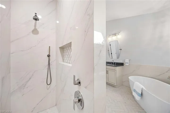 Bathroom with a soaking tub, a marble finish shower, vanity, tile walls, and a wainscoted wall
