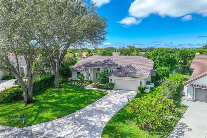 View of front facade with stucco siding, driveway, a front yard, a tile roof, and a water view