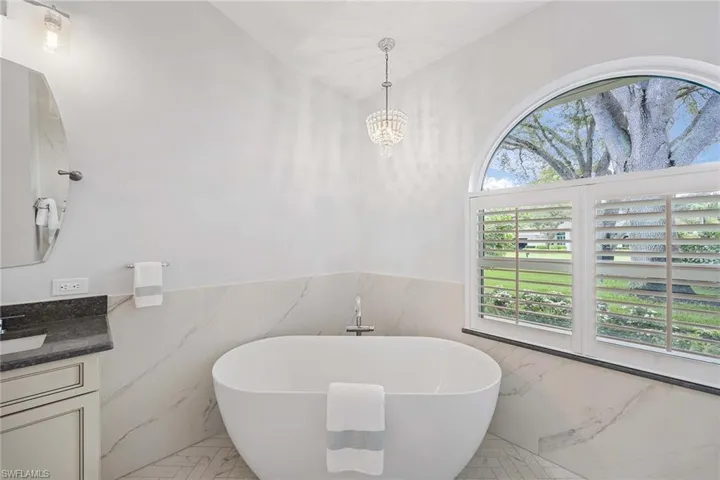Bathroom with a wainscoted wall, a freestanding tub, tile walls, light marble finish floors, and vanity