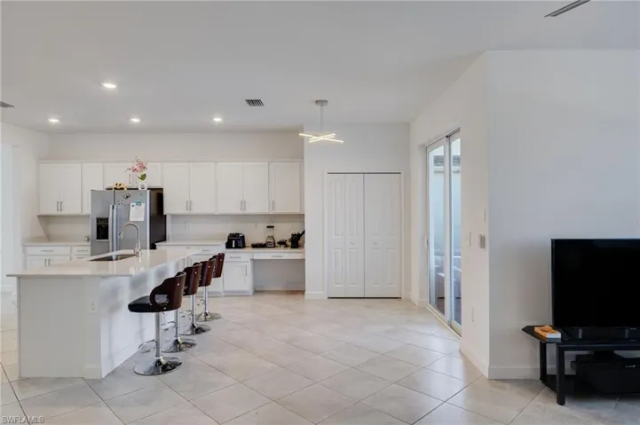 Kitchen featuring white cabinets, a breakfast bar, stainless steel fridge, a kitchen island with sink, and light stone countertops