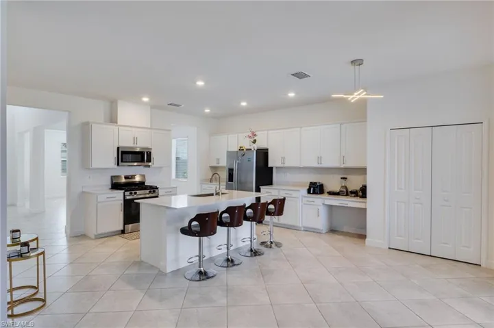 Kitchen featuring a kitchen bar, stainless steel appliances, white cabinets, light tile patterned floors, and a center island with sink