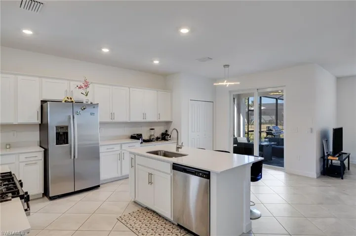 Kitchen with stainless steel appliances, decorative light fixtures, white cabinetry, and an island with sink