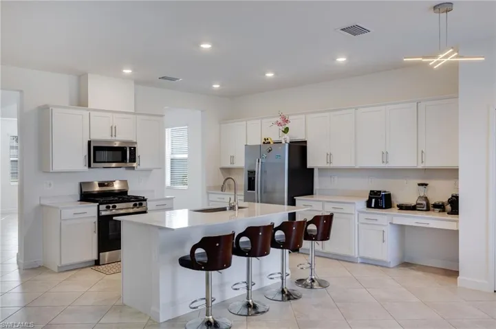 Kitchen featuring stainless steel appliances, white cabinetry, a breakfast bar area, a center island with sink, and decorative light fixtures
