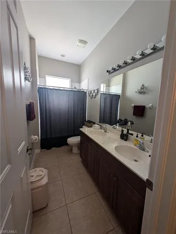 Bathroom with double vanity, light tile patterned floors, and a shower with curtain