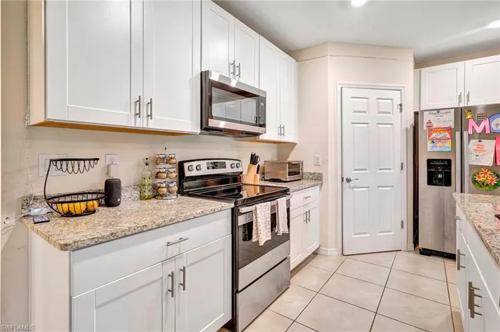 Kitchen featuring light stone countertops, light tile floors, white cabinetry, and appliances with stainless steel finishes