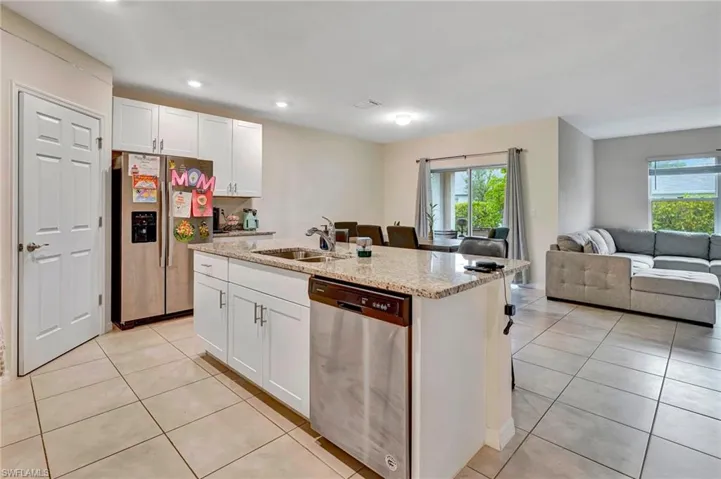Kitchen with white cabinetry, light stone countertops, appliances with stainless steel finishes, an island with sink, and light tile floors