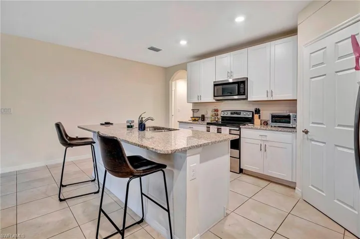 Kitchen featuring a kitchen island with sink, white cabinetry, appliances with stainless steel finishes, sink, and light tile floors