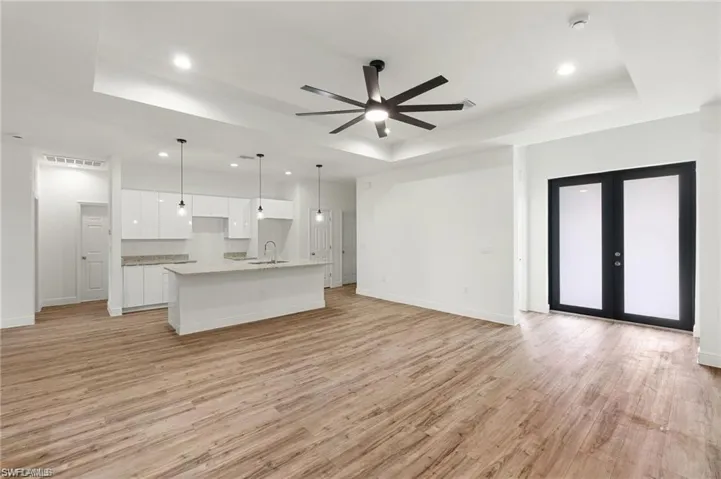 Unfurnished living room featuring a tray ceiling, sink, french doors, light hardwood / wood-style floors, and ceiling fan