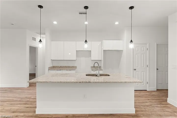 Kitchen with white cabinets, light hardwood / wood-style flooring, a center island with sink, and sink
