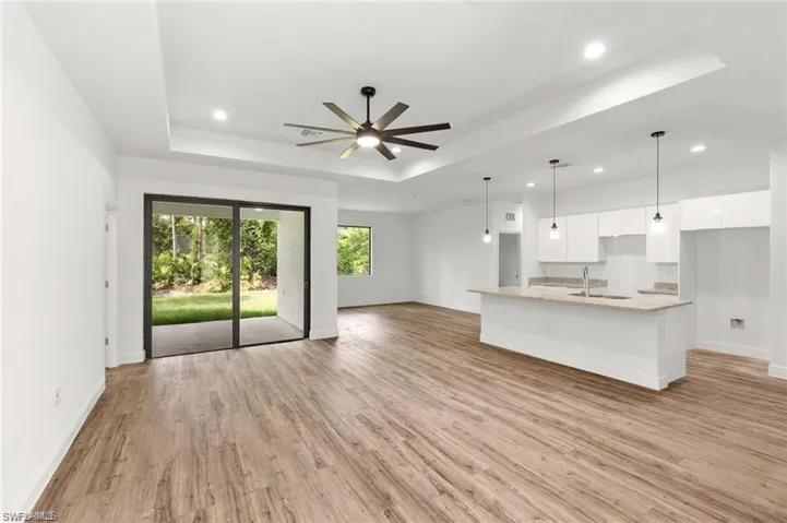 Unfurnished living room featuring light hardwood / wood-style floors, sink, ceiling fan, and a tray ceiling