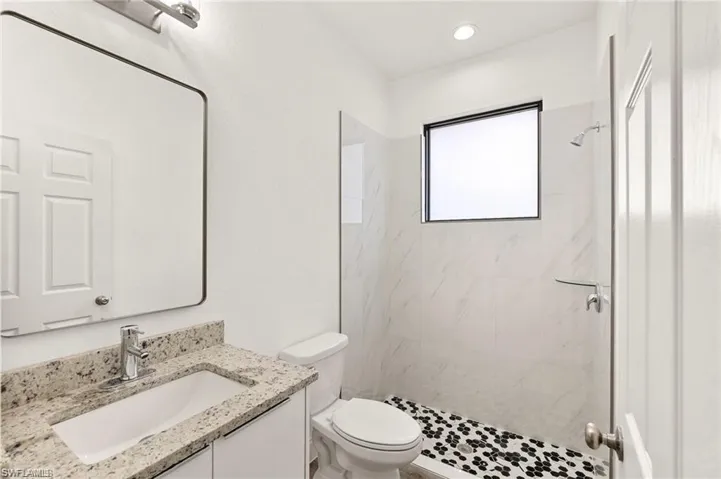 Bathroom with tiled shower, toilet, and vanity